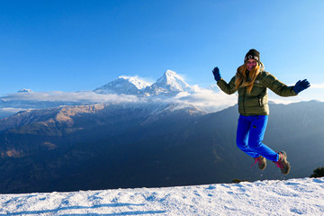 Girl is jumping in front of the mountains. White clouds. Green forest.