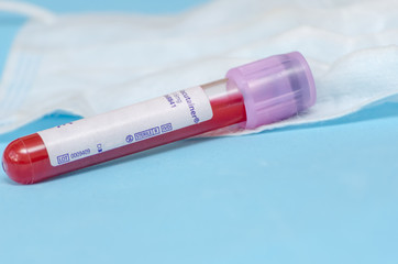 test tube with blood lies on the background of a medical mask close up on a blue background