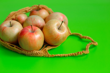 Juicy ripe red-yellow apples lie in a knitted bag on a green background