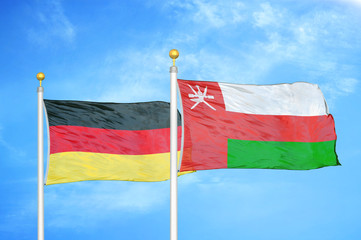 Germany and Oman two flags on flagpoles and blue cloudy sky