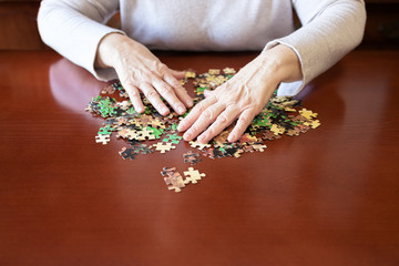 Old woman hands and jigsaw puzzle pieces on a table