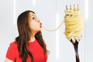 Young woman sucks huge pasta and spaghetti from a big fork