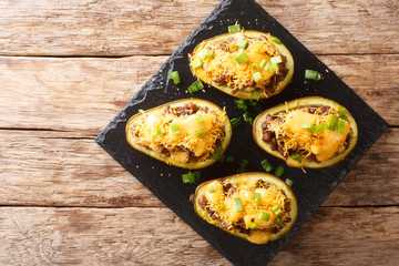 Ripe baked avocados with minced meat, onions and cheddar cheese close-up on a slate board. horizontal top view