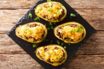 Freshly baked avocado with minced meat, onions and cheddar cheese close-up on a slate board. horizontal top view
