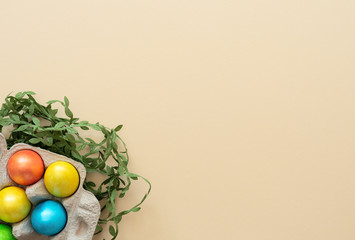Decorated Easter eggs lie in the carton box on yellow background with green leaves. Happy Easter...