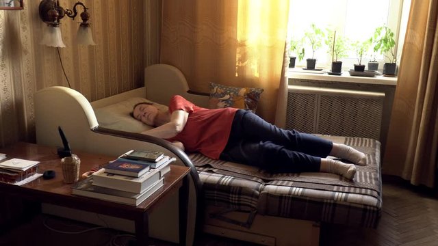 An elderly woman sleeps on the couch during the day. First on his back, then turns on his side.