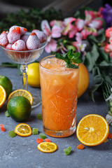 Summer fresh cold drink beverages. Ice Lemonade in the jug and lemons and orange with mint on the table outdoor. Orange lemonade in a glass.