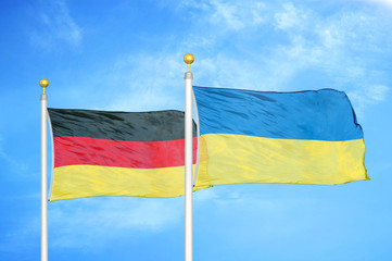 Germany and Ukraine two flags on flagpoles and blue cloudy sky