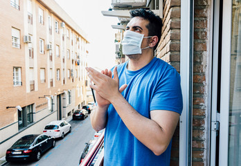 Young man with mask applauding people who are fighting against coronavirus (covid19) from the...