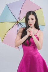 Portrait of happy beautiful young  asian woman  wearing pink dress holding umbrella, smiling in  studio on white background.