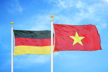 Germany and Vietnam two flags on flagpoles and blue cloudy sky
