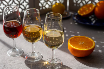 Glasses with cold dry fino and sweet cream sherry fortified wine and orange in sunlights, andalusian style interior on background
