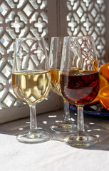 Glasses with cold dry fino and sweet cream sherry fortified wine and orange in sunlights, andalusian style interior on background