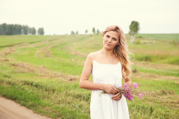Fototapeta na wymiar outdoor portrait of a beautiful middle aged blonde woman in a field with flowers.