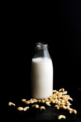 Vegan Cashew Milk in bottle with raw cashews on black surface