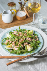 Arugula and trout salad with egg and asparagus on a plate on a table covered with a tablecloth with a glass of wine and a glass of water, sauceboat and butter vertical arrangement