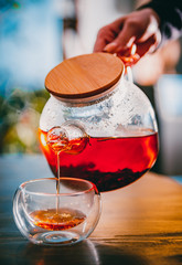 Pouring tea from a glass teapot into a cup on table in cafe