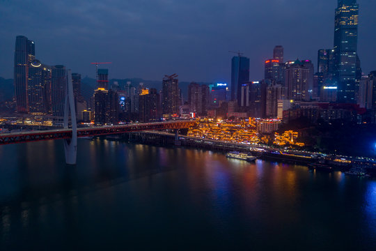Aerial dusk view of Hong Ya dong Cave, Historic Chinese folk religion town with light on by Jialing River skyscrapers