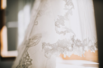 closeup of white elegant fashionable bride dress hanging in bright room