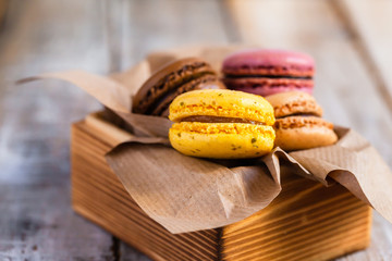 Assortment of delicious traditional french macaroons. Colorful sweet dessert for real gourmands. Lemon, chocolate, caramel, raspberry flavors. Wooden rustic background, craft paper, close up, macro
