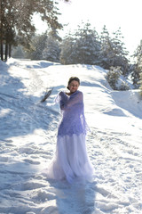 Fototapeta na wymiar vertical portrait of a cute European woman in a long white dress and a light purple openwork shawl against the winter landscape