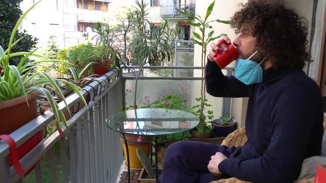 Europa, Italy , Milan - Man 40 years old with mask in quarantine at home - Smart work in apartment drinking milk coffe on the balcony foro breakfast