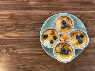Homemade blueberry pudding in foil molds on a turquoise plate with orange physalis on a wooden table. Copy space