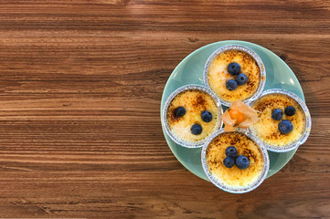 Blueberry pudding in foil molds on a turquoise plate with orange physalis on a wooden table. Copy space