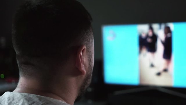 Bearded Caucasian man watching jailbait video on TV screen at home