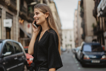 Young woman looks startled receiving some information by the call on her phone. She listen to the audio message and became happy hearing the voice of her friend. Girl is crossing the road.