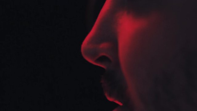 Close up of a man's nose and mouth as he sneezes with a black background and moody red lighting.