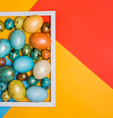 Colored Easter eggs in a wooden white frame and next to it on a colored background. Happy Easter!