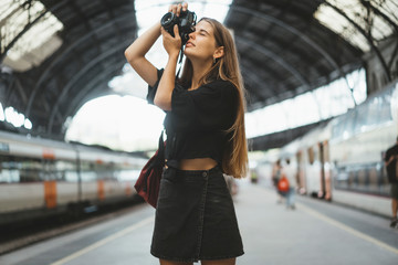 A young girl is a tourist who visits different cities and takes photos of different urban views. At the railway station, a nice young lady with a camera in her hands takes pictures