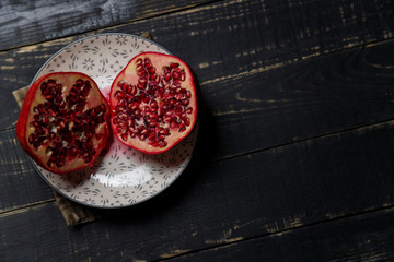 Two halves of pomegranate fruit on plate on black wooden background. Copy space