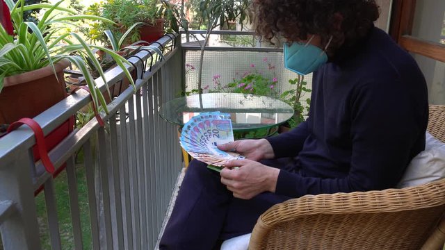 Italy , Milan - Man 40 years old with mask in quarantine at home - Smart work in apartment - GOVERNMENT STATE AID MONEY COMING SOON IN SUPPORT OF POVERTY CAUSED BY  EPIDEMIC - COUNTING MONEY EURO INPS