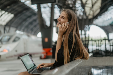 Girl is holding her smartphone and accepting a call. Young blonde woman is sitting on the stone...