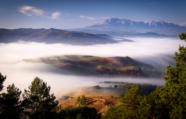 Beautiful, colorful autumn panorama of Pieniny Mountains (Male Pieniny) in the fog and morning light with Tatra Mountains in the background. 
Poland, Slovakia.