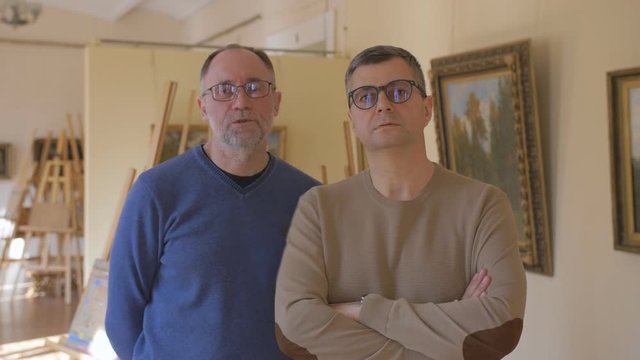 Two intelligent men in an art gallery look at a picture and talk about art
