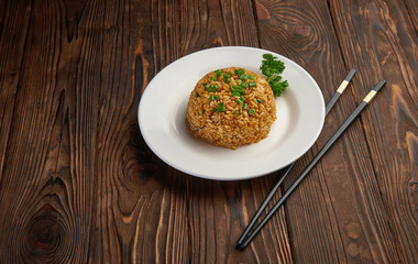 Asian style fried rice with fresh onion and sliced carrot, pairs of chopsticks on dark wooden background copy space, oriental food concept top view