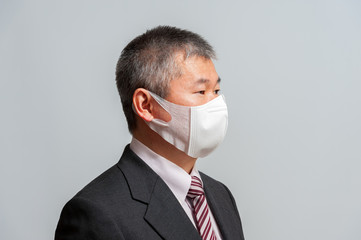 Side view of middle aged Asian man with suit and tie wearing white face mask for protection against Coronavirus (COVID-19). Isolated on white background. Looking to the side.