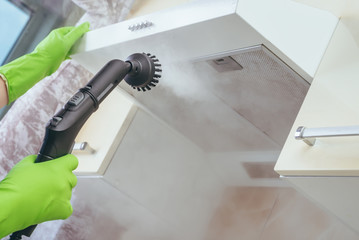 house cleaning. Girl brushes steam cleaners kitchen drawing with steam in green gloves. cleaning of...