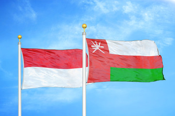 Indonesia and Oman two flags on flagpoles and blue cloudy sky