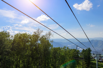 Lift in the mountains on sunny day. Mountain valley with cable car, view from top. Green vegetation in the Altai mountains. Concept of summer vacation.