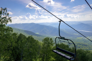 Lift on the background of mountains and green hills on sunny summer day. Empty bench of ski lift, tourism closed off quarantine. Inactive resorts.