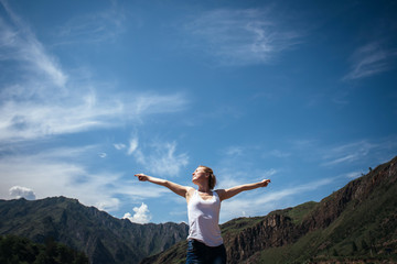 Happy female traveller in a white t-shirt against the beautiful mountains and blue sky on sunny day. Cheerful young girl enjoying a trip in the Altai mountains.