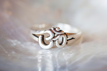 Obraz na płótnie Canvas Silver ring tiny jewelry piece on white pearl background in the shape of om