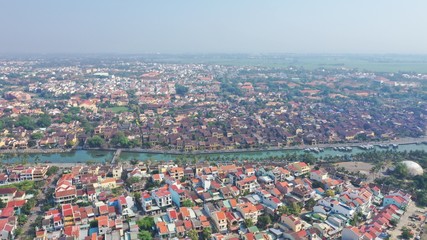 Fototapeta na wymiar Aerial view of Hoi An old town on Thu Bon river, Quang Nam province, Vietnam. Unesco world heritage. Boats moored to river embankment. Bridge. Many roof tops.