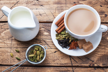 Indian drink masala tea with milk and spices. Cardamom sticks cinnamon star anise cane sugar. Wooden background copy space.