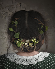 spring female portrait from the back in a vintage dress with a lace collar, with a hairstyle decorated with flowering plants and flowers with a composition of small quail eggs, stylized as a bird nest
