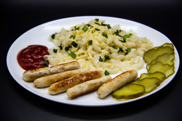 Pasta on a plate with cheese on top and green onions. Delicious pasta made from high quality flour with chicken sausage from grill and sliced cucumber from jar. Horns made of flour cooked with cheese